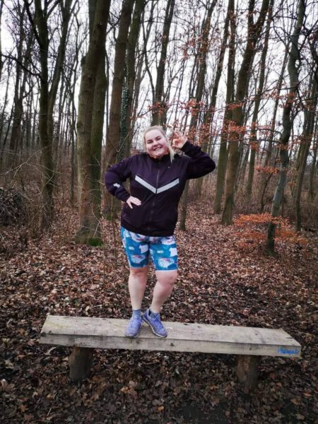 Kobieta w czarnej bluzie i niebieskich szortach na drewnianej kładce w lesie
