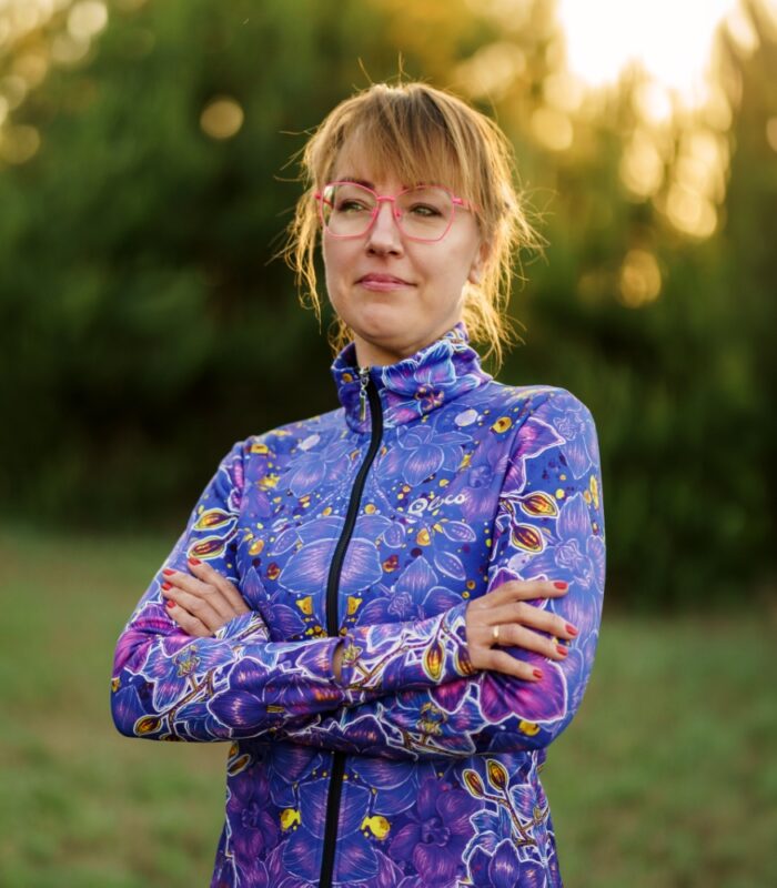 Modelka w bluzie damskiej Nocna Orchidea LOCO ze skrzyżowanymi rękami, widoczny kwiatowy wzór na przodzie i rękawach.