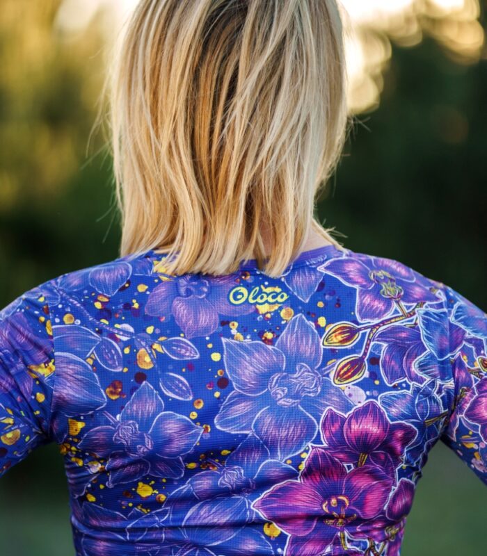 Zbliżenie górnej części pleców longsleeve’u Nocna Orchidea LOCO, widoczne żółte logo pod dekoltem i fioletowo-niebieskie orchidee.